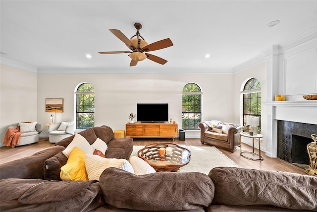 living room with a premium fireplace, crown molding, ceiling fan, and light hardwood / wood-style flooring