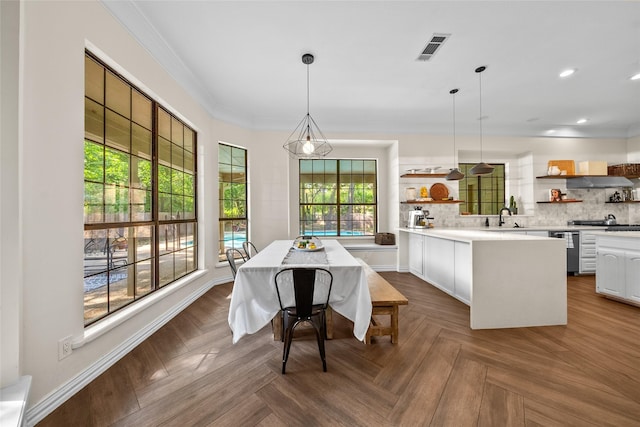 kitchen with dark parquet flooring, kitchen peninsula, crown molding, decorative light fixtures, and white cabinetry