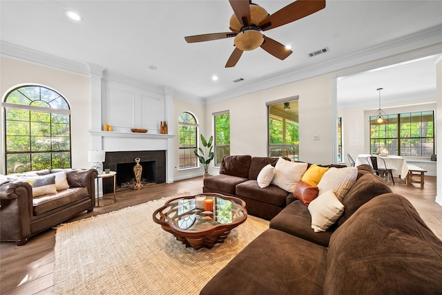 living room featuring ceiling fan, a high end fireplace, ornamental molding, and light wood-type flooring