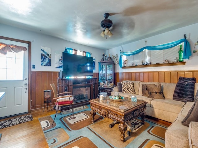 living room with a fireplace, hardwood / wood-style floors, ceiling fan, and wood walls