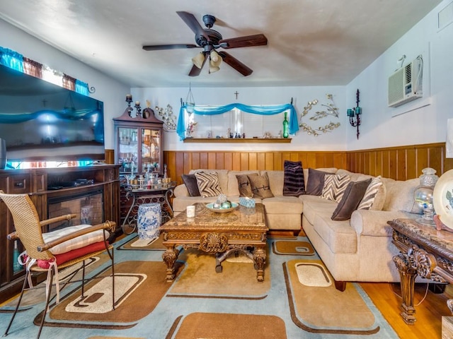 living room with a wall mounted air conditioner, ceiling fan, wooden walls, wood-type flooring, and a fireplace