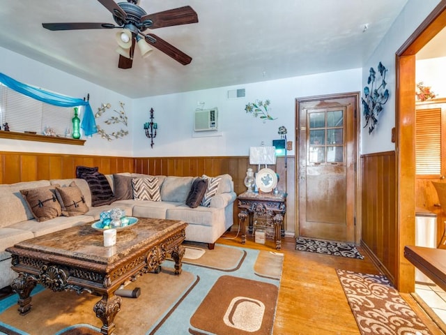 living room featuring a wall mounted air conditioner, light wood-type flooring, ceiling fan, and wood walls