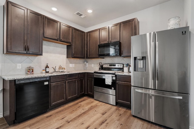 kitchen featuring sink, light stone counters, light hardwood / wood-style flooring, dark brown cabinets, and black appliances