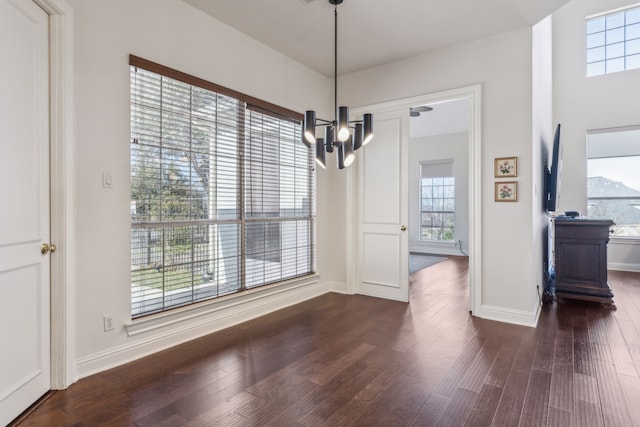 unfurnished dining area with a chandelier, baseboards, and dark wood finished floors