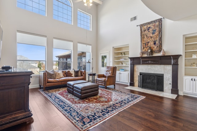 living room featuring visible vents, a fireplace, a towering ceiling, wood finished floors, and built in features