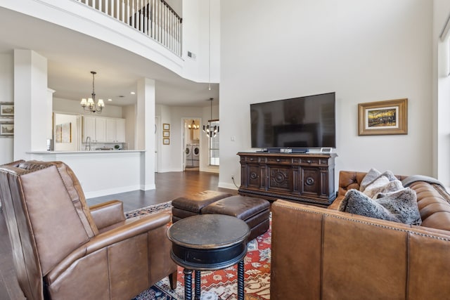 living room with wood finished floors, washer and dryer, baseboards, a notable chandelier, and a towering ceiling