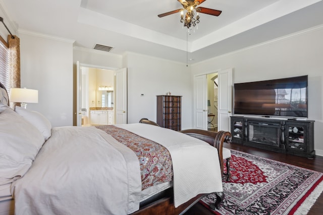 bedroom featuring connected bathroom, a raised ceiling, visible vents, and wood finished floors
