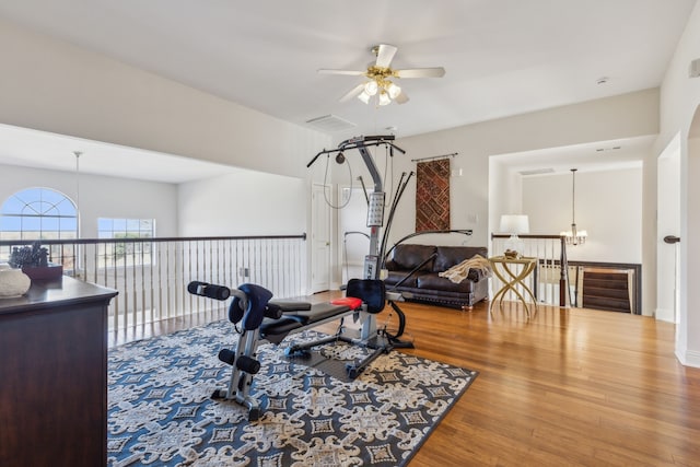 exercise room featuring wood finished floors and ceiling fan with notable chandelier