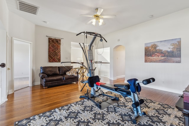 exercise room with ceiling fan, visible vents, baseboards, arched walkways, and wood finished floors