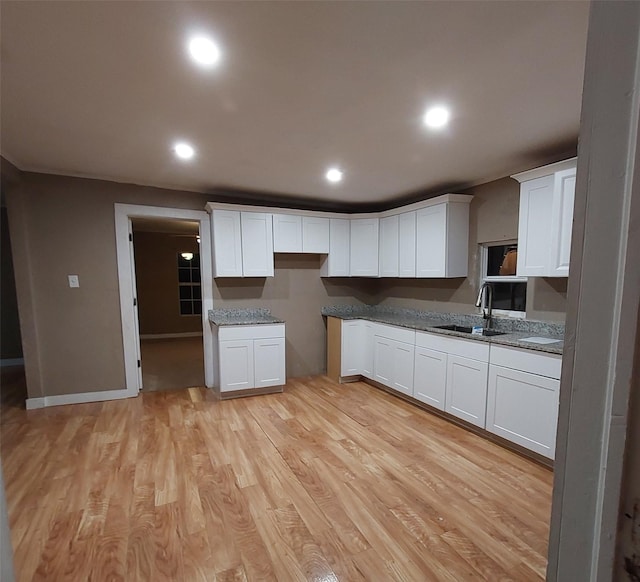 kitchen with white cabinetry, sink, light stone counters, and light wood-type flooring