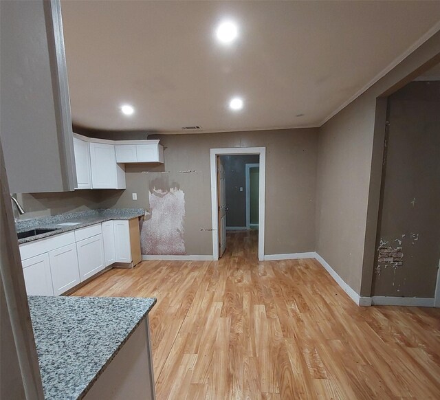 kitchen with light stone countertops, sink, white cabinetry, and light hardwood / wood-style floors