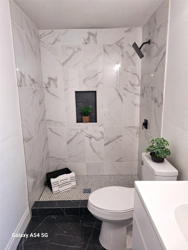 bathroom featuring a tile shower, vanity, and toilet