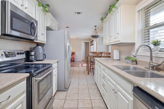 kitchen with white cabinets, sink, light tile patterned floors, appliances with stainless steel finishes, and decorative light fixtures