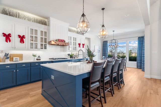 kitchen with pendant lighting, white cabinets, blue cabinets, an island with sink, and stainless steel gas cooktop