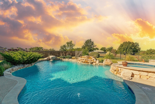 pool at dusk featuring an in ground hot tub