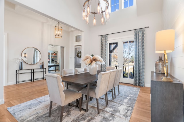 dining room featuring french doors, a towering ceiling, a notable chandelier, and light wood-type flooring