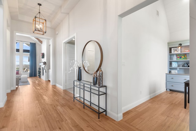 corridor with light wood-type flooring, an inviting chandelier, and high vaulted ceiling