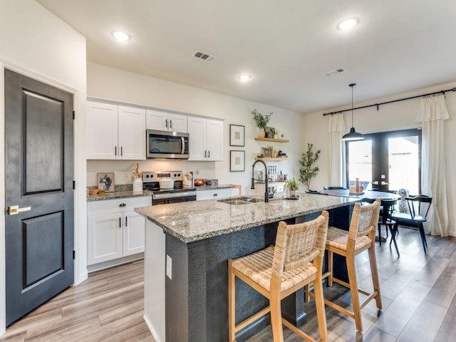 kitchen with white cabinets, appliances with stainless steel finishes, a kitchen island with sink, and sink