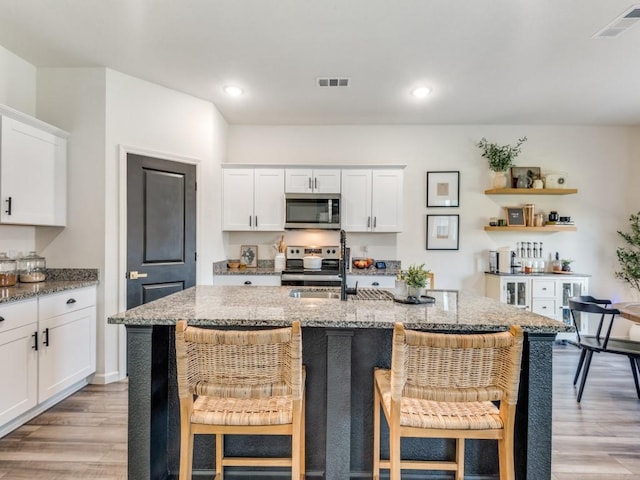 kitchen with a breakfast bar, stainless steel appliances, white cabinetry, and a kitchen island with sink