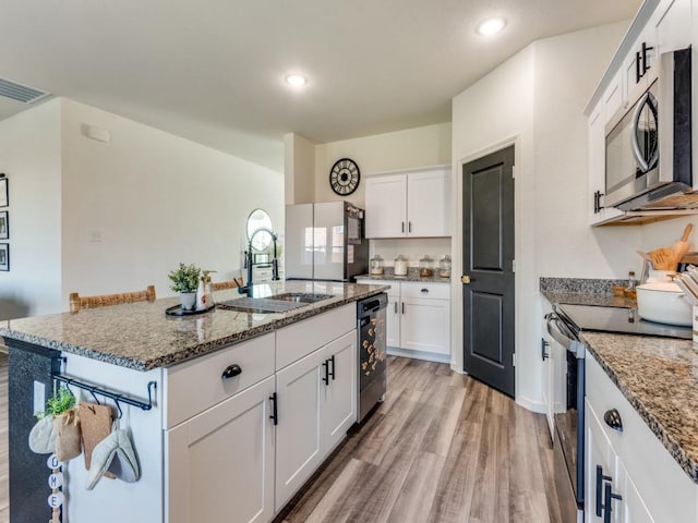 kitchen featuring white cabinetry, sink, stone countertops, a kitchen island with sink, and appliances with stainless steel finishes