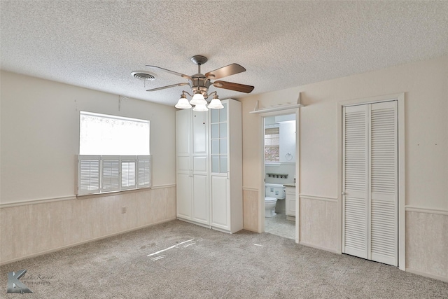 unfurnished bedroom featuring ensuite bath, ceiling fan, light colored carpet, a textured ceiling, and wooden walls