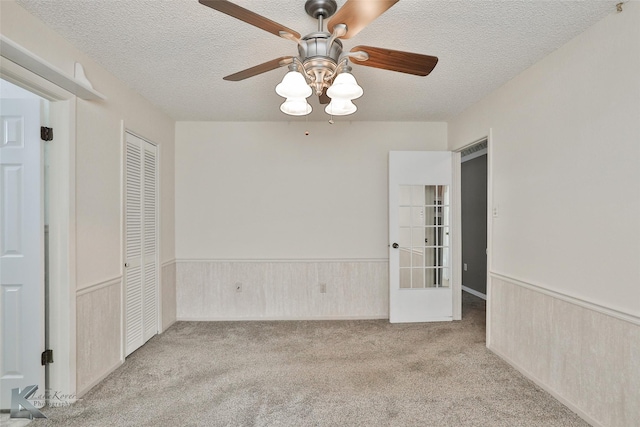 carpeted empty room featuring ceiling fan, french doors, a textured ceiling, and wooden walls