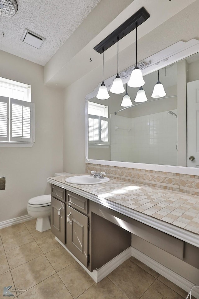 bathroom with vanity, tile patterned floors, toilet, tiled shower, and a textured ceiling