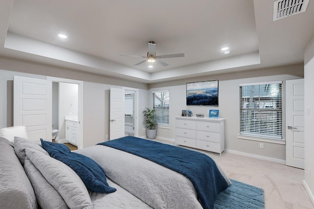 bedroom featuring ensuite bathroom, ceiling fan, a tray ceiling, and light colored carpet