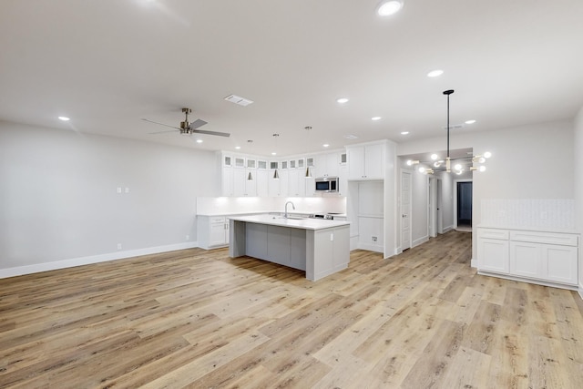 kitchen featuring ceiling fan, decorative light fixtures, a center island with sink, white cabinets, and light wood-type flooring