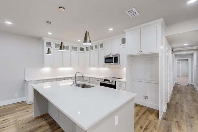 kitchen featuring appliances with stainless steel finishes, sink, decorative light fixtures, a center island with sink, and white cabinetry