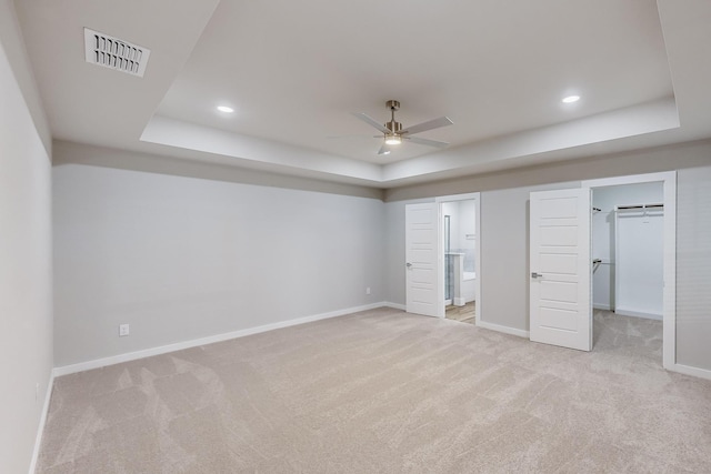 unfurnished bedroom with light carpet, ensuite bathroom, a raised ceiling, and ceiling fan