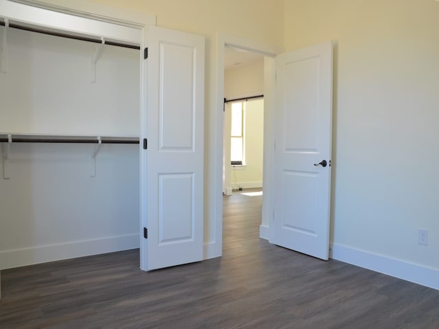 unfurnished bedroom featuring dark wood-type flooring, a barn door, and a closet