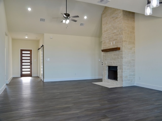 unfurnished living room with ceiling fan, high vaulted ceiling, dark hardwood / wood-style floors, a fireplace, and a barn door