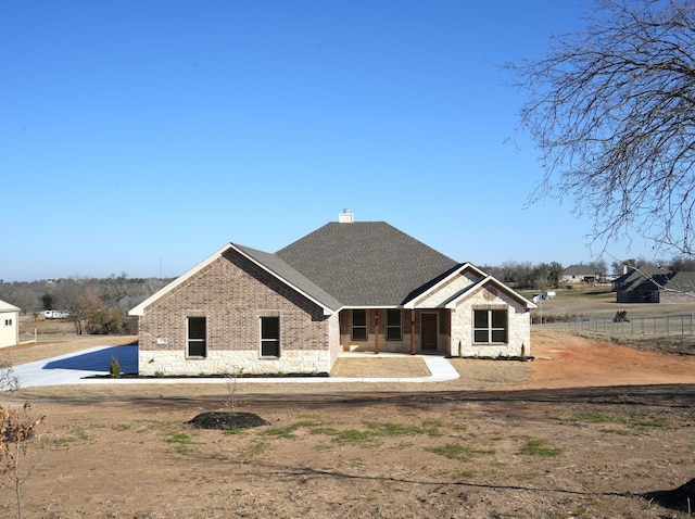 view of front facade with brick siding, a shingled roof, fence, stone siding, and a chimney