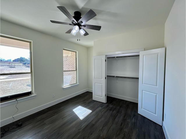 unfurnished bedroom with multiple windows, dark wood-type flooring, ceiling fan, and a closet