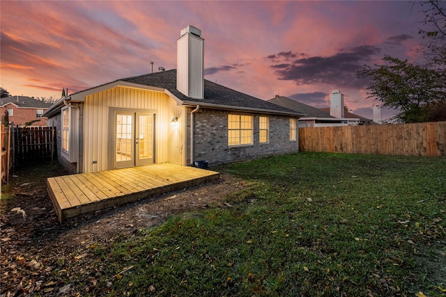 back house at dusk featuring french doors, a wooden deck, and a lawn