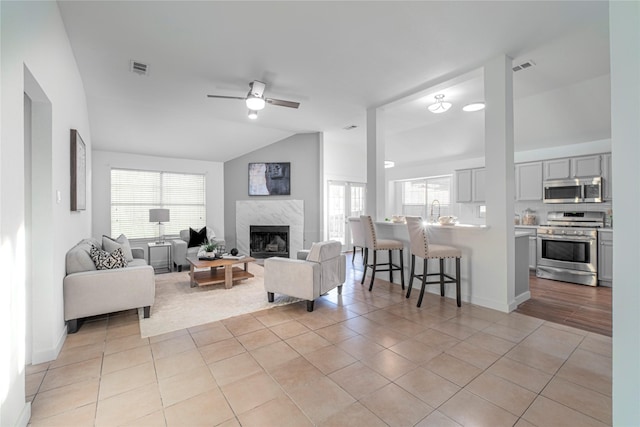 living room with a high end fireplace, vaulted ceiling, ceiling fan, light tile patterned floors, and a healthy amount of sunlight