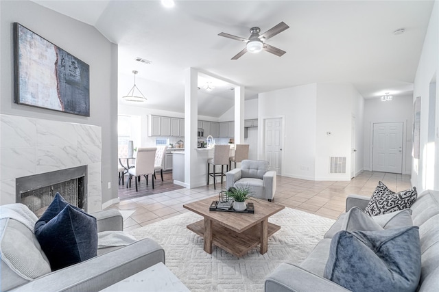 living room with a high end fireplace, ceiling fan, light tile patterned floors, and vaulted ceiling