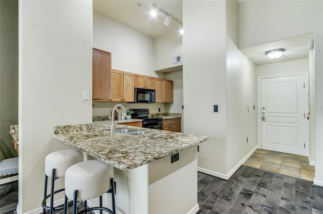 kitchen featuring a kitchen bar, sink, kitchen peninsula, a towering ceiling, and black appliances