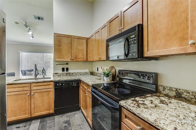 kitchen featuring sink, light stone counters, ornamental molding, black appliances, and light wood-type flooring