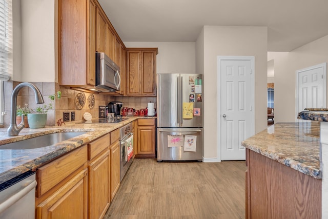 kitchen with sink, tasteful backsplash, stainless steel appliances, light stone countertops, and light hardwood / wood-style floors