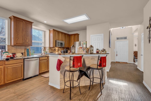 kitchen featuring sink, a breakfast bar area, decorative backsplash, stainless steel appliances, and light hardwood / wood-style flooring