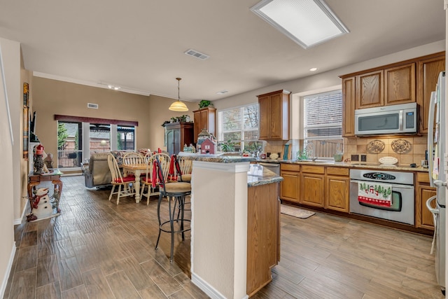 kitchen with a kitchen island, appliances with stainless steel finishes, decorative light fixtures, backsplash, and a kitchen breakfast bar