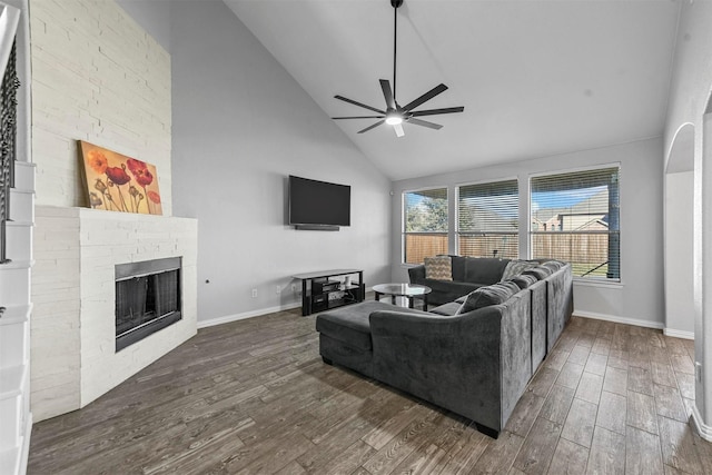 living room featuring a stone fireplace, ceiling fan, high vaulted ceiling, and dark wood-type flooring