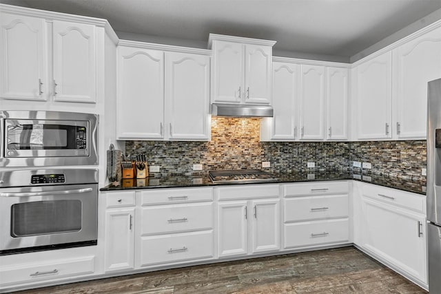 kitchen with white cabinets, backsplash, stainless steel appliances, and dark stone countertops