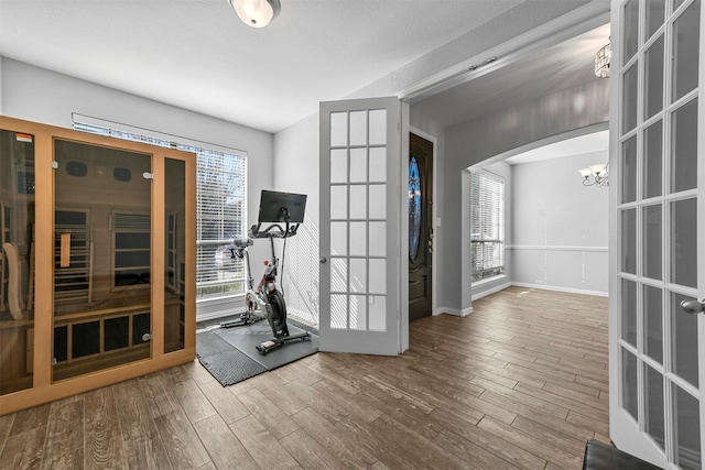 exercise room featuring a notable chandelier, wood-type flooring, and french doors