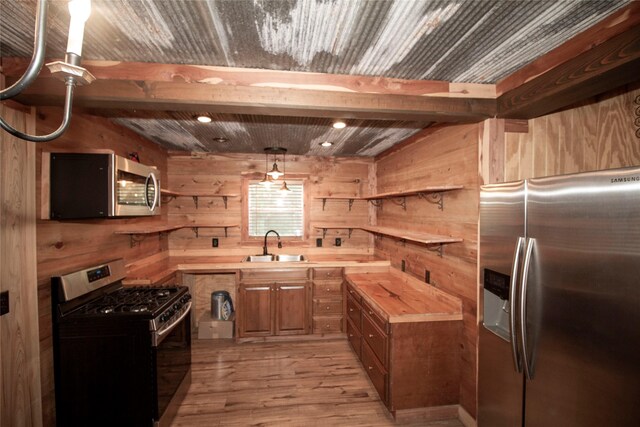 kitchen with appliances with stainless steel finishes, wooden walls, sink, butcher block countertops, and hanging light fixtures