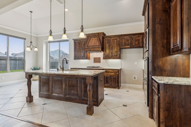 kitchen featuring light stone countertops, premium range hood, sink, pendant lighting, and a center island with sink