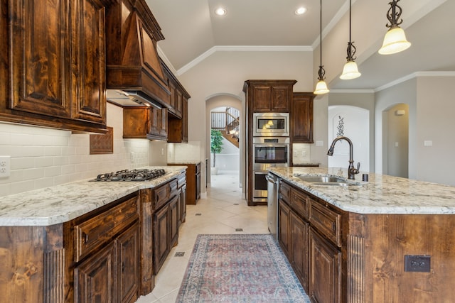 kitchen with sink, an island with sink, pendant lighting, vaulted ceiling, and appliances with stainless steel finishes