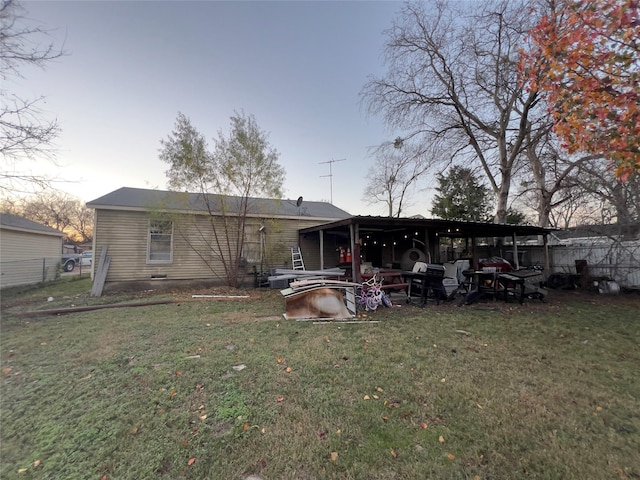 back house at dusk featuring a lawn and a carport